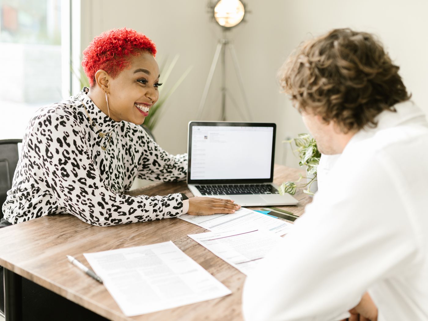 Two people going through printed statements together at a desk, a laptop open beside them